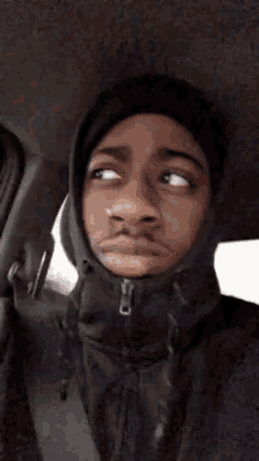 a man wearing a hooded jacket and a hat is sitting in a car .