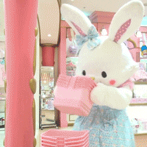 a stuffed bunny mascot in a pink and blue dress is holding a pink basket
