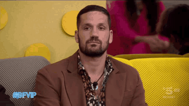 a man with a beard is sitting on a yellow couch with the hashtag #gfvip on the bottom