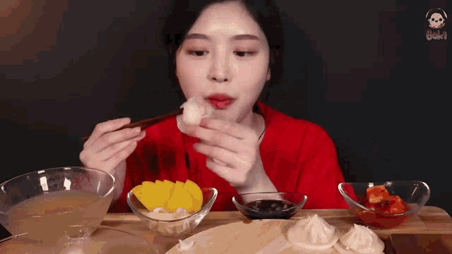 a woman is eating a dumpling with chopsticks while sitting at a table with bowls of food .