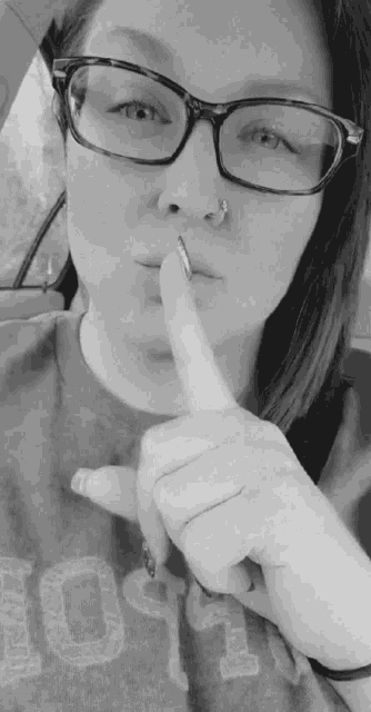 a woman wearing glasses and a nose ring is holding her finger to her mouth