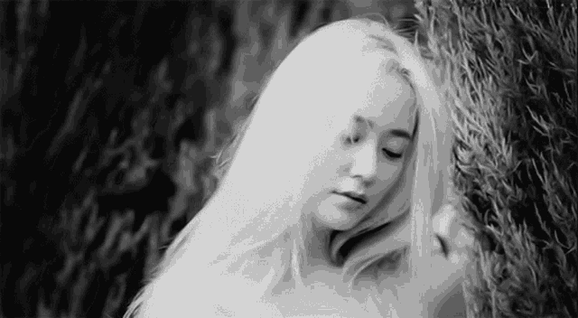 a woman with white hair is leaning against a tree in a black and white photo .