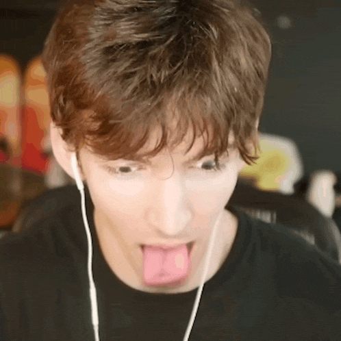 a young man is sticking his tongue out while wearing ear buds .