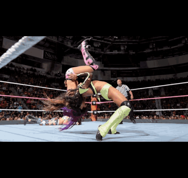 two women wrestling in a ring with a referee and a sign that says wwe