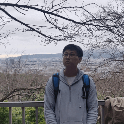 a man wearing glasses and a backpack is standing in front of a city