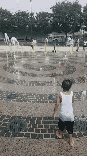 a boy in a white tank top is playing in a water fountain