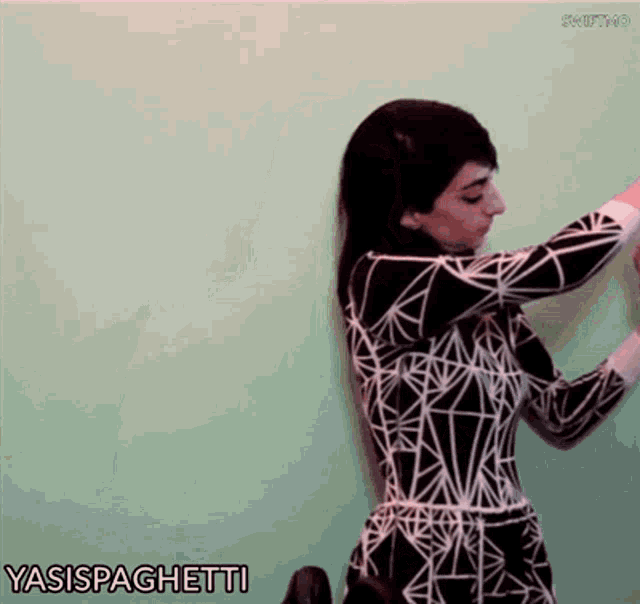 a woman in a black and white dress is standing in front of a green wall and says yasispaghetti