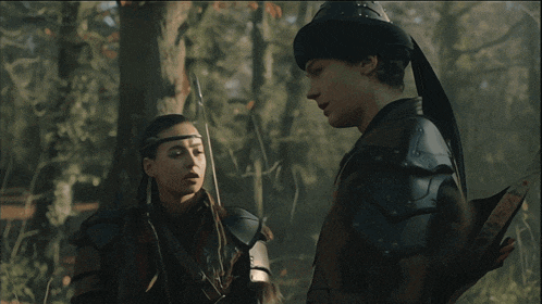 a man and a woman are standing next to each other in a dark forest