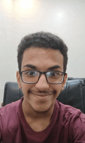 a young man wearing glasses and a maroon shirt takes a selfie