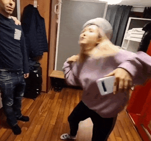 a woman in a purple sweater is holding a cell phone while dancing