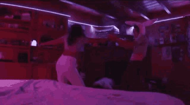 a couple of women are standing next to each other on a bed in a room with purple lights .