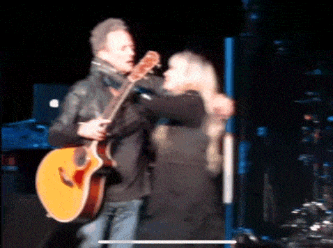 a man is holding a guitar while a woman is hugging him on stage .