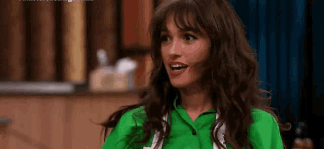 a woman with long hair and bangs is wearing a green shirt and smiling at the camera .