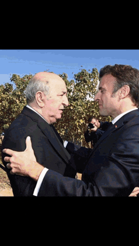 two men in suits are hugging each other with trees in the background