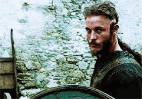 a man with a beard and long hair is holding a shield and looking at the camera .