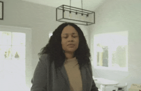 a woman is standing in a living room with her eyes closed and making a face .