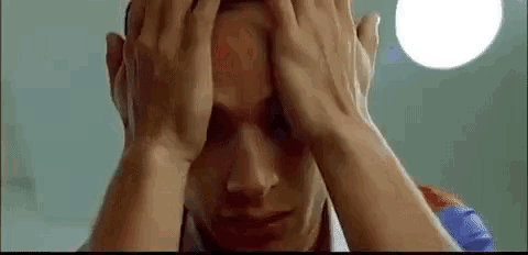 a man is covering his face with his hands and has a bloody spot on his forehead .