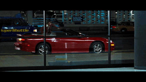 a red car is parked in front of a supershuttle bus