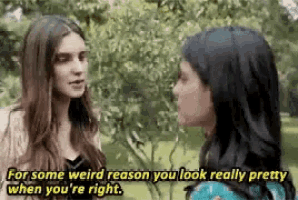 two women are standing next to each other in a park and talking .