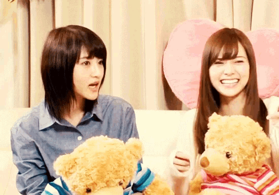 two women sitting on a couch holding teddy bears and smiling