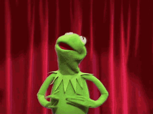 kermit the frog is standing in front of a red curtain with a giant hand behind him