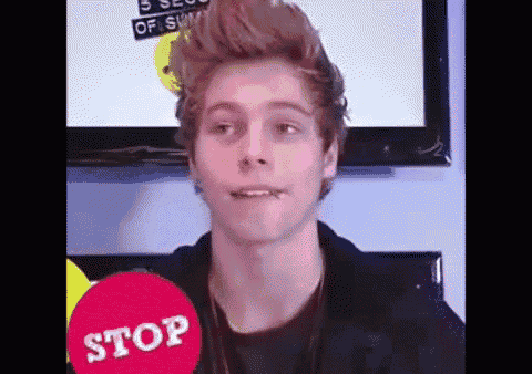 a young man is making a funny face in front of a television while holding a stop sign .