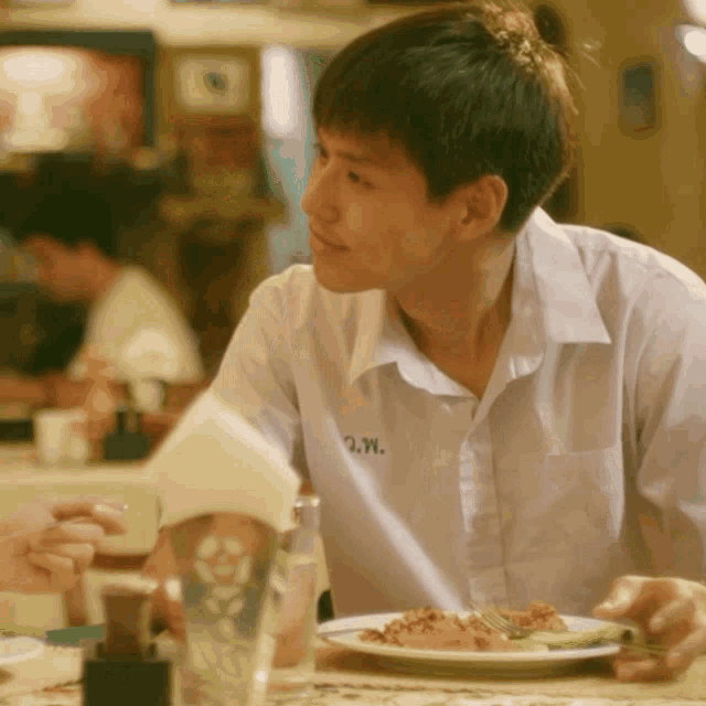 a young man sitting at a table with a napkin and a plate of food with the letter w on his shirt