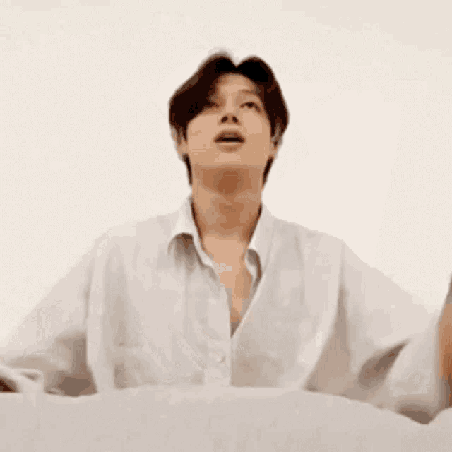a man in a white shirt is standing in front of a white wall with his hands in the air .