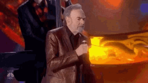 a man in a suit is singing into a microphone while standing next to a piano .