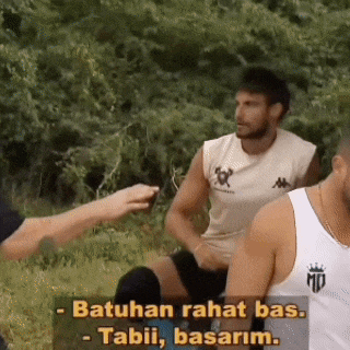 a group of men are sitting in the grass and one of them is talking to another man .