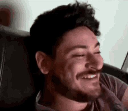 a man with a beard is smiling with his eyes closed while sitting on a couch .