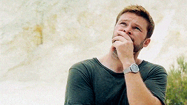 a man with a watch on his wrist is covering his mouth with his hand while looking up .