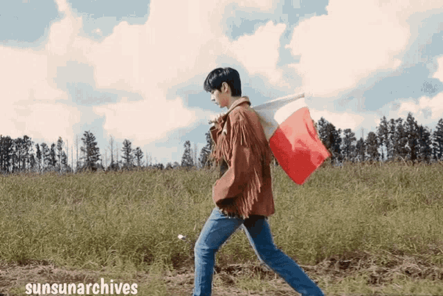 a man carrying a red and white flag in a field with sunsunarchives written on the bottom right