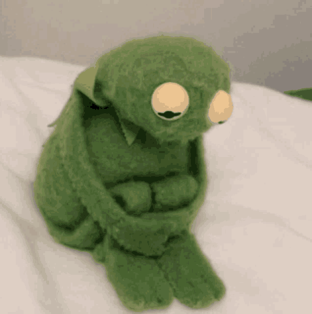 a kermit the frog stuffed animal is sitting on a bed