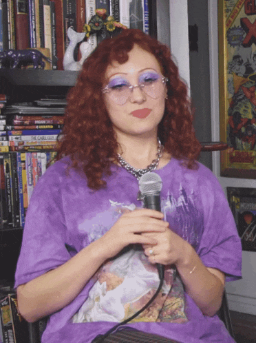 a woman in a purple shirt holds a microphone in front of a shelf of dvds