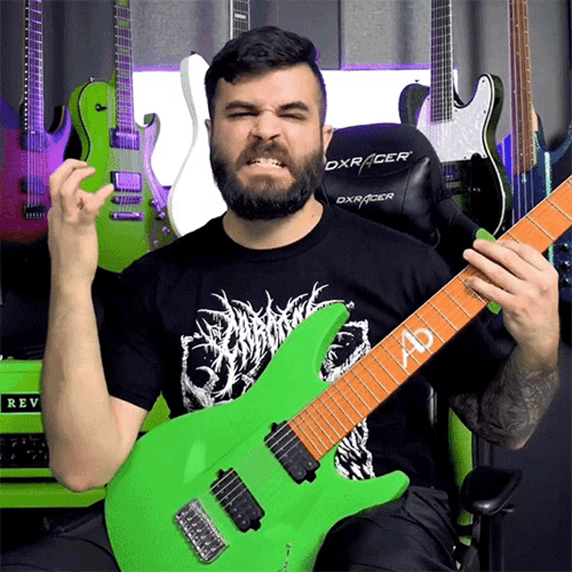 a man with a beard is playing a green guitar in front of a black dxracer chair