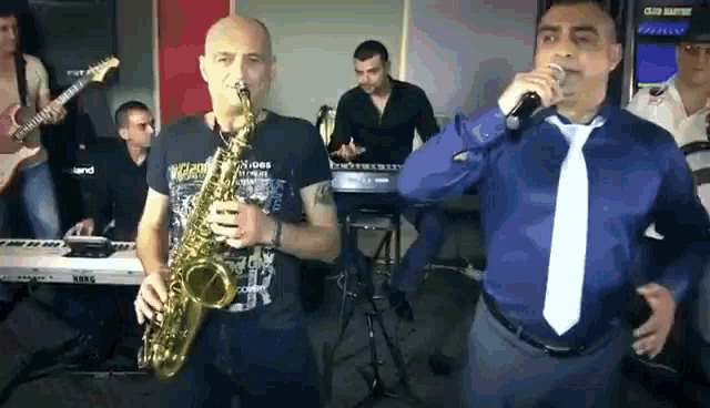 a man playing a saxophone next to another man singing into a microphone .