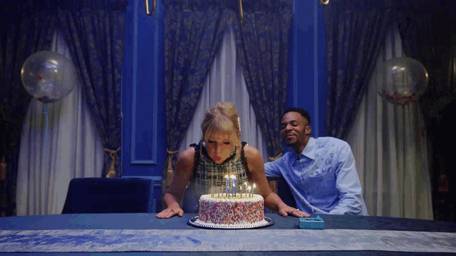 a woman blowing out candles on a birthday cake with sprinkles