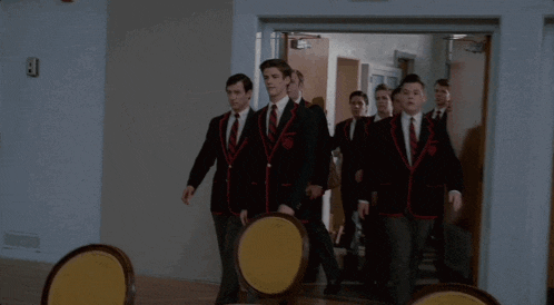 a group of young men in suits and ties are walking through a hallway