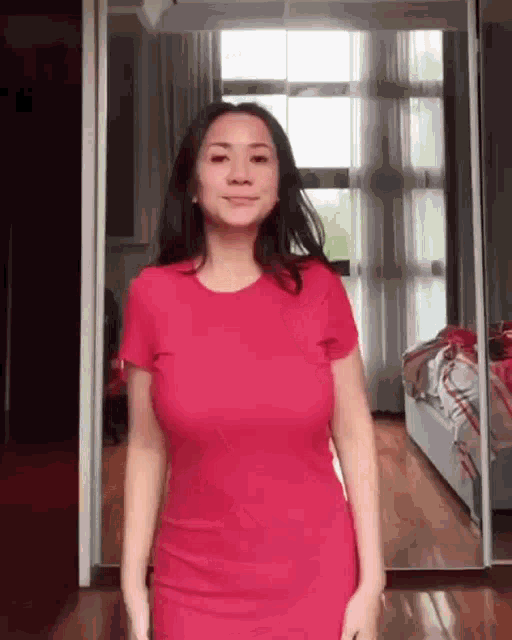 a woman in a red dress is standing in a room in front of a mirror .