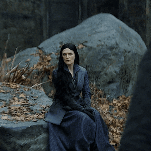 a woman in a blue dress sits on a large rock