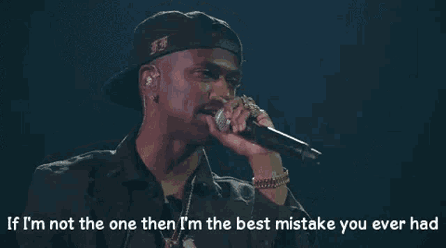 a man is holding a microphone in his hand and singing into it while wearing a hat .