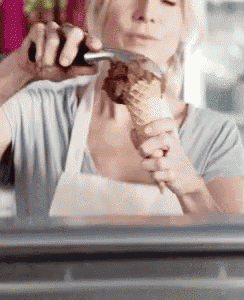 a woman in an apron is eating an ice cream cone with a spoon .