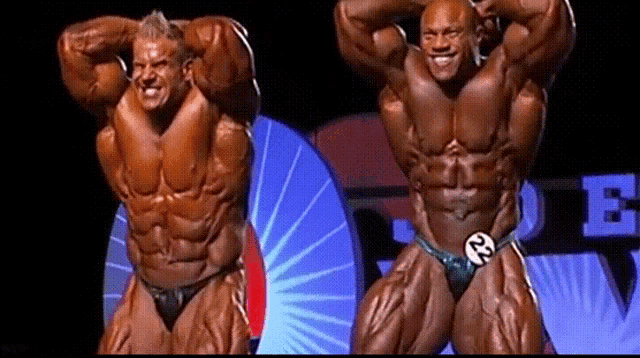 two bodybuilders are posing for a picture and one of them has the number 22 on his shorts
