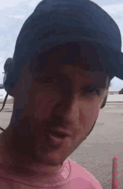a man wearing a pink shirt and a black hat is talking