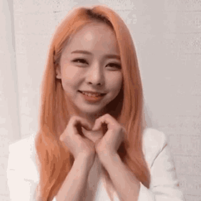 a young woman with orange hair is making a heart shape with her hands .