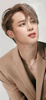a young man wearing a suit and a necklace is looking at the camera .
