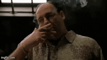 a man is smoking a cigarette while drinking a glass of whiskey .