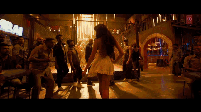 a woman in a white dress stands in front of a crowd in a bar with a sign that says raw