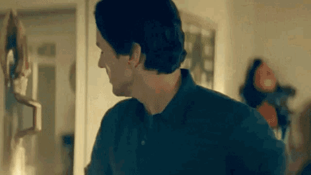 a man in a blue shirt is standing in a room looking at a mirror .